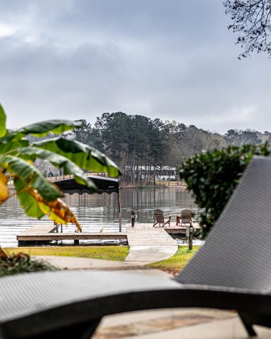 Rectangular swimming pool with lounge chairs and safety fence, surrounded by tall pine trees and lake view beyond